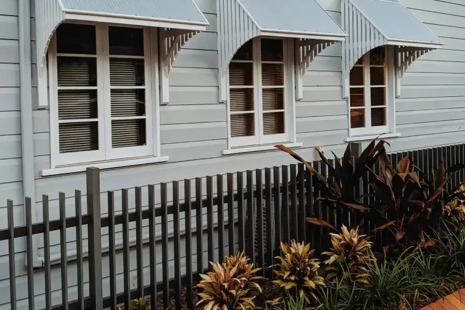 A house with three windows and a fence.